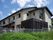 白い外壁に黒い屋根が付いた一般の住宅を大きく使用な外観のホーム。建物の周りにはフェンスが建てられ、緑の草木がある。