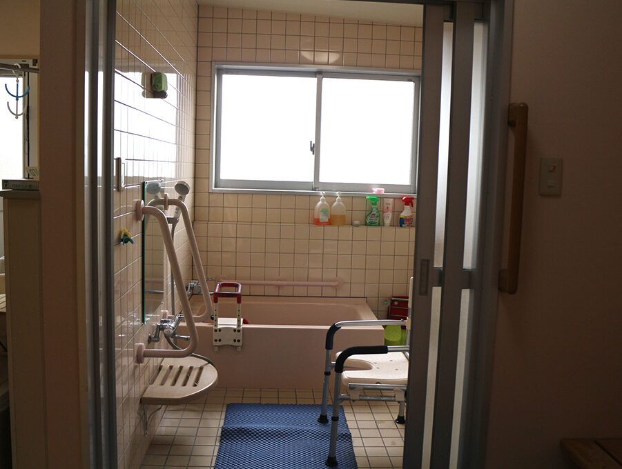 眼鏡をかけた高齢男性が福祉車両から下りようとしているところを若いスタッフが手伝っている。