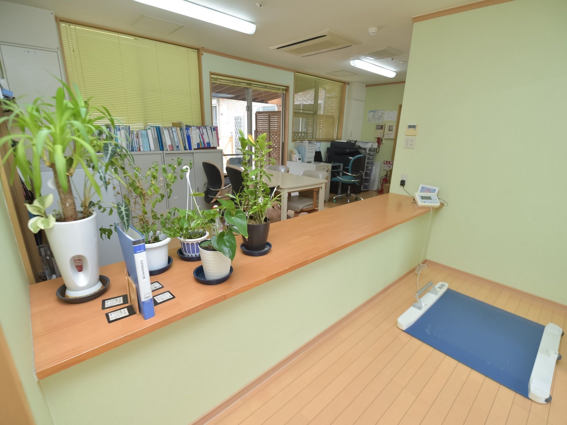 事務室には血圧計など健康をチェックする装置が置かれている。後ろの棚の上には、たくさんのファイルが並んでいる。