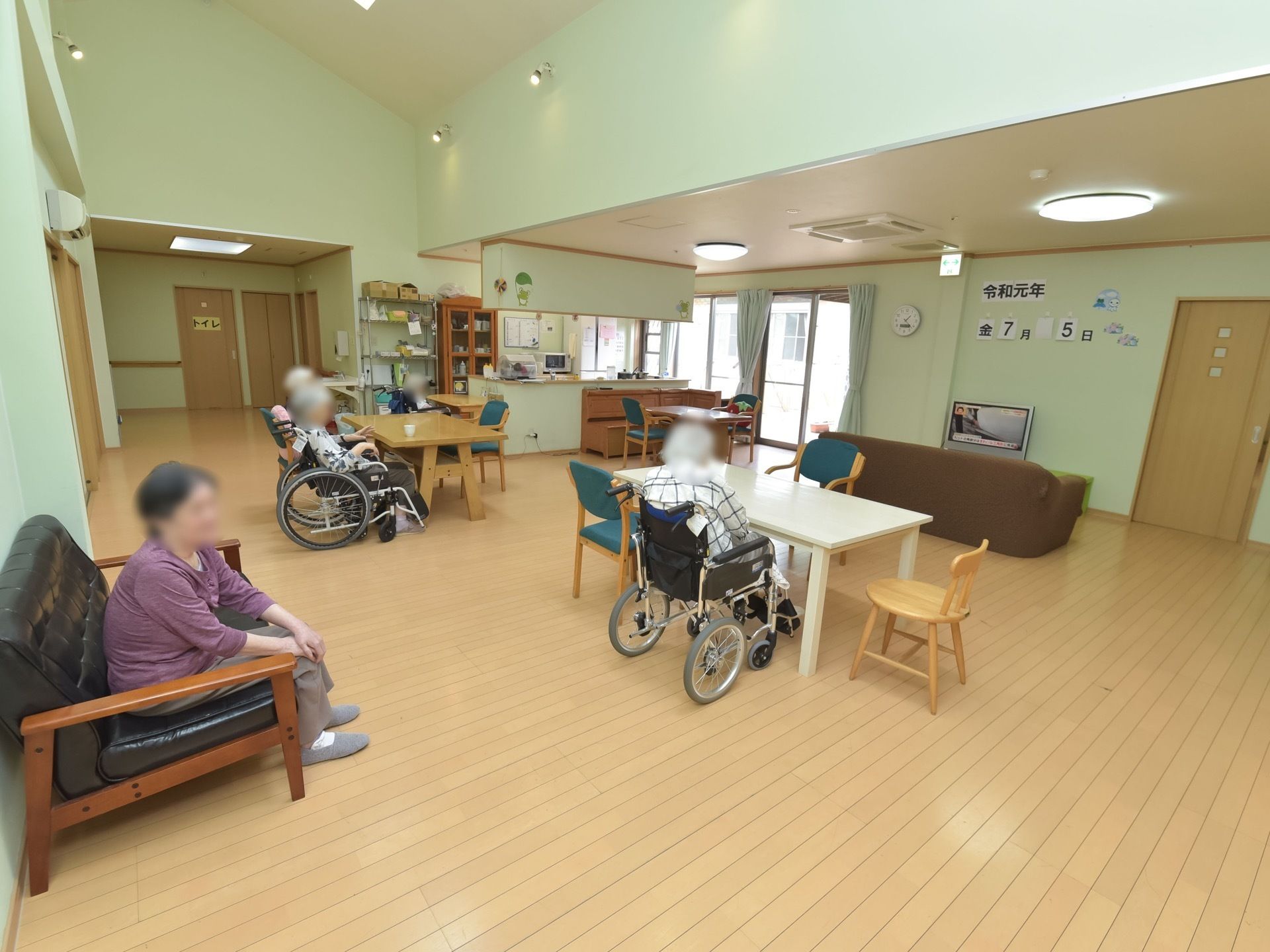 車椅子をご利用の入居者様も気軽に過ごせるよう、共有スペースのテーブルは間隔をあけて置かれている。壁際にはテレビがある。