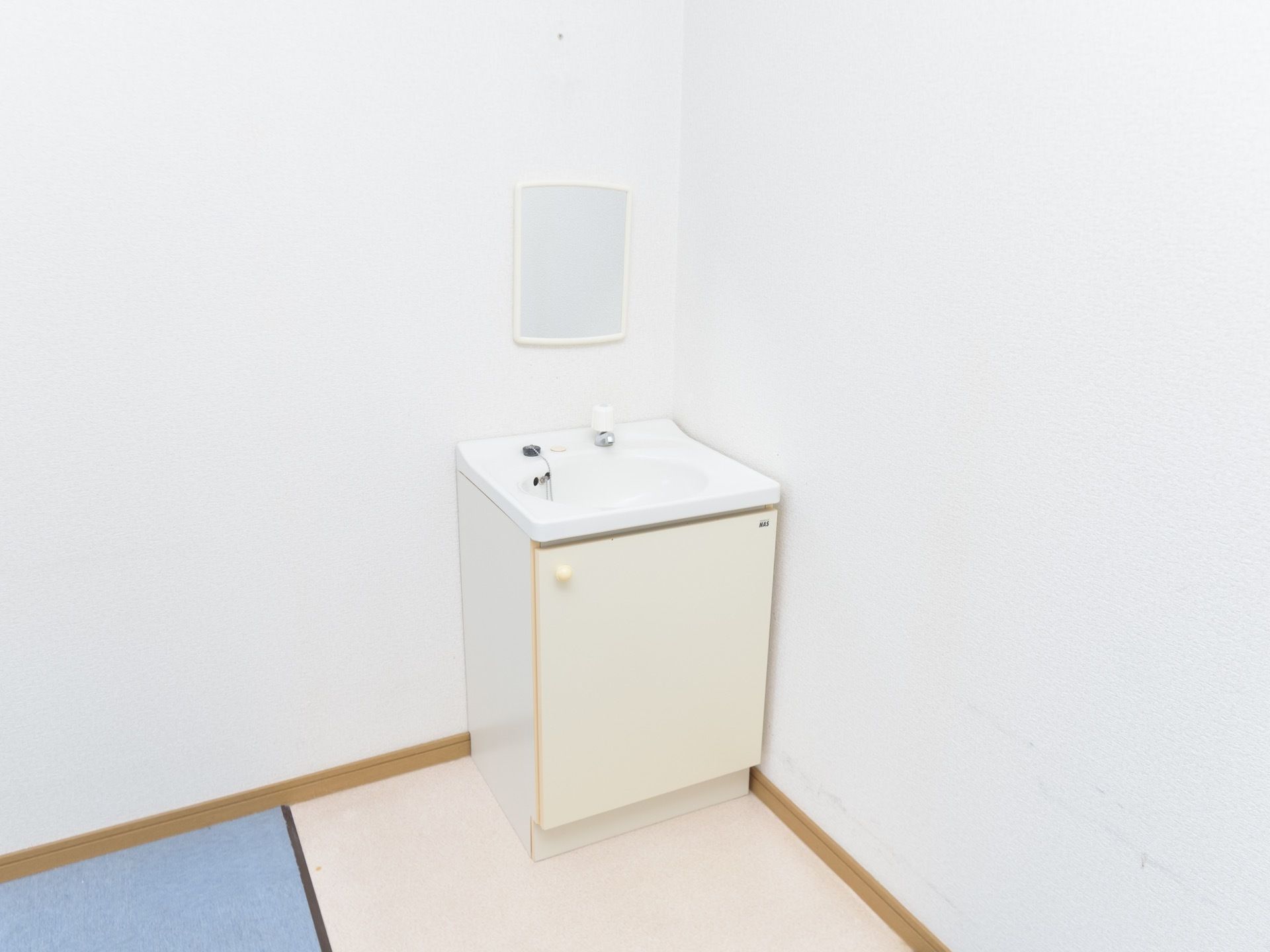 洋風の部屋の角に、洗面台が１つ備え付けられている。また、洗面台の上方の壁には、鏡も１枚設置されている。