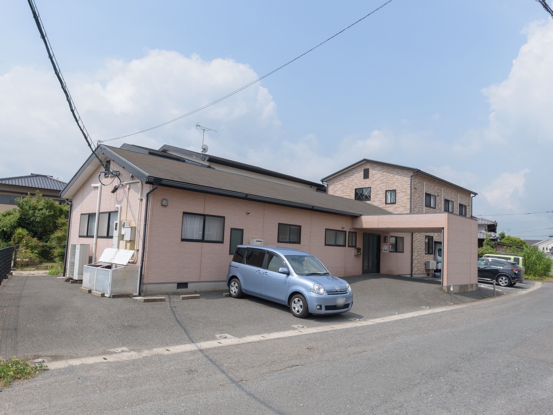 青い車が前に停まっている2階建てのグループホーム