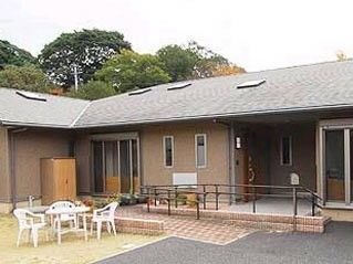 ブラウンの平屋建ての建物の前には花が植えられ、手すりが付き、階段とスロープもある。