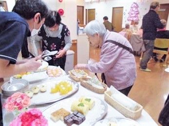 レースペーパーの上にケーキがたくさん並べられた皿を指し、ケーキを取ってもらっている入居者。