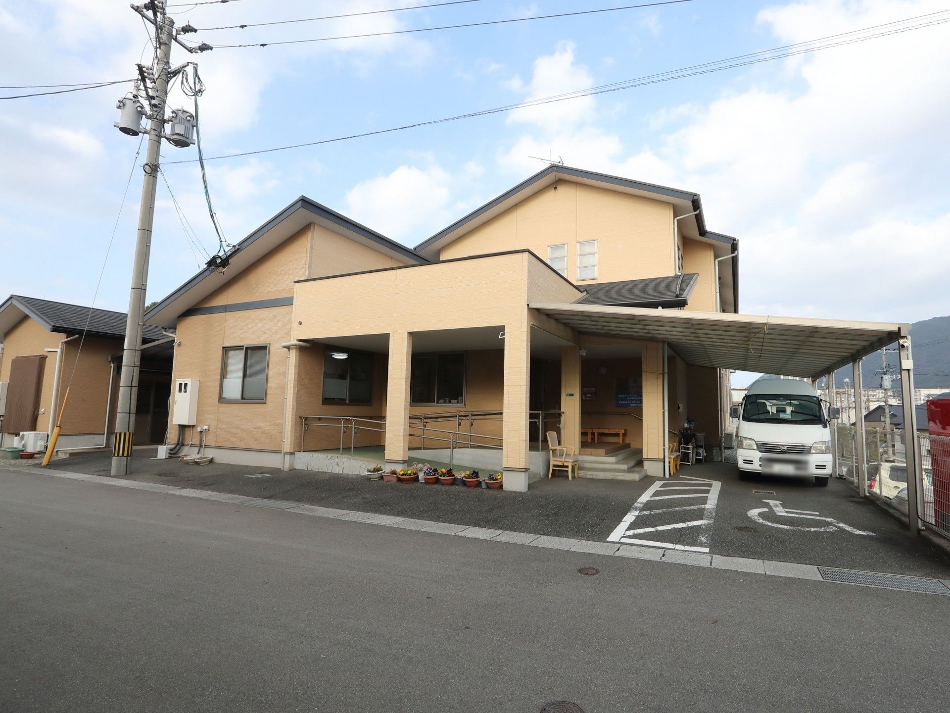 車いすに座った高齢の男女がエプロンを付けた若い男女のスタッフに付き添われ屋外で笑顔で過ごしている。