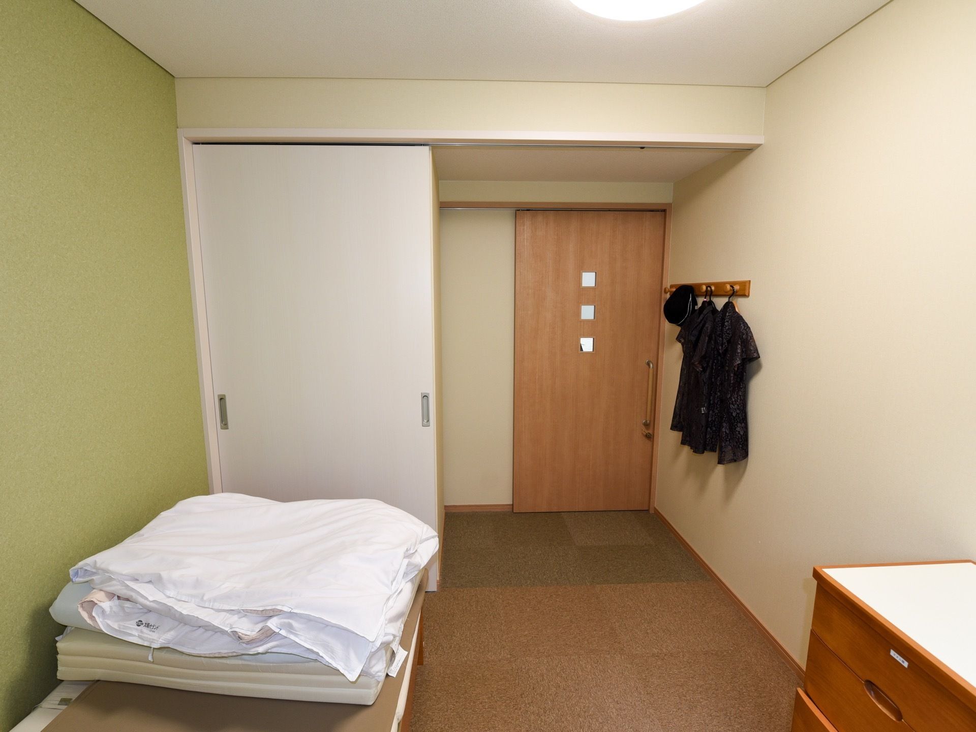 洋室タイプの居室である。介護ベッドや照明、ハンガーフックが完備されている。壁際に収納家具が置かれている。