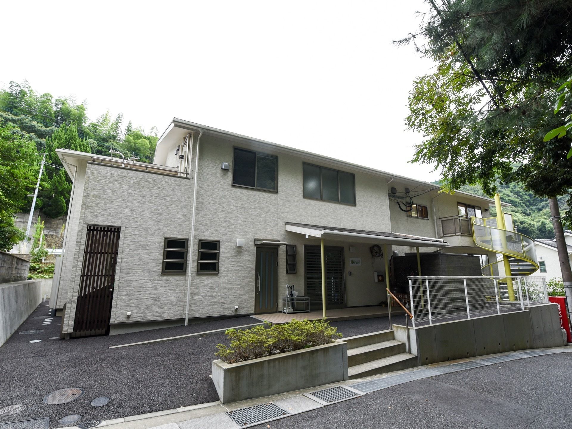 白い外壁の２階建て施設である。螺旋階段が設置されている。建物前の出入り口には、手すり付きの階段が設けられている。