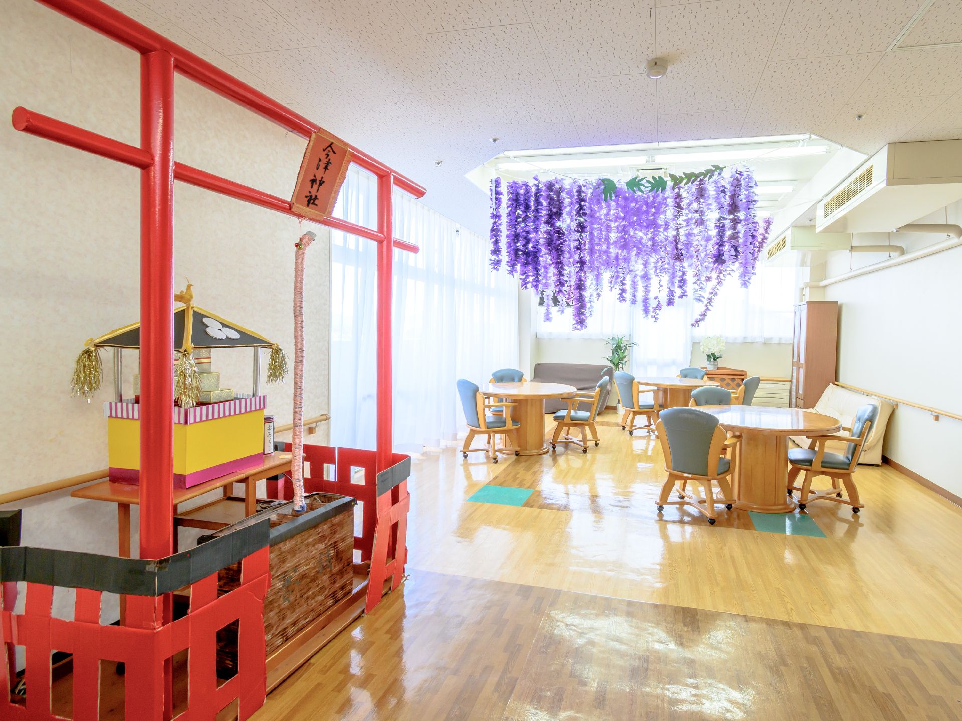 緑の多い屋外で笑顔で過ごしている車いすの高齢男性と付き添いのエプロンを付けた若い女性スタッフ。