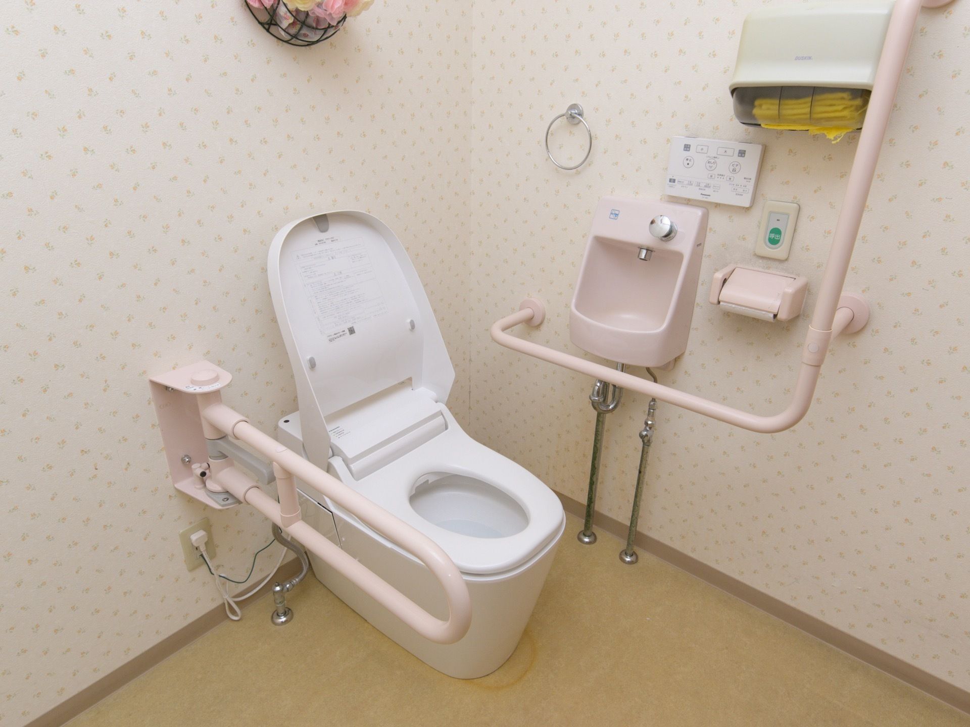 白を基調とした清潔感あふれるトイレで、手洗い場が設けられている。便座の両サイドには手すりが設置されている。