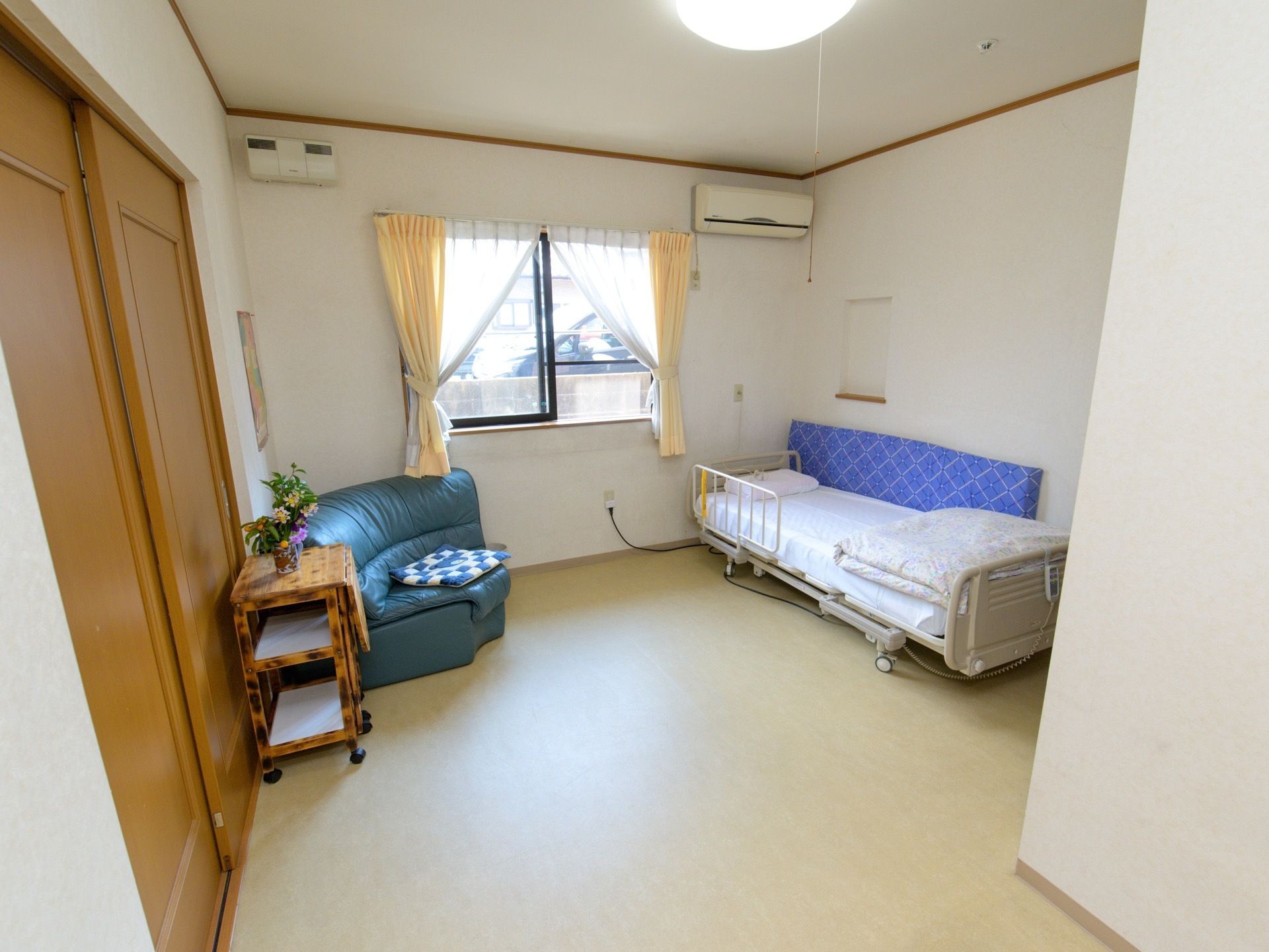 白を基調としたシンプルなワンルームの居室。壁にはエアコンが設置されており、ソファやベッドが置かれている。