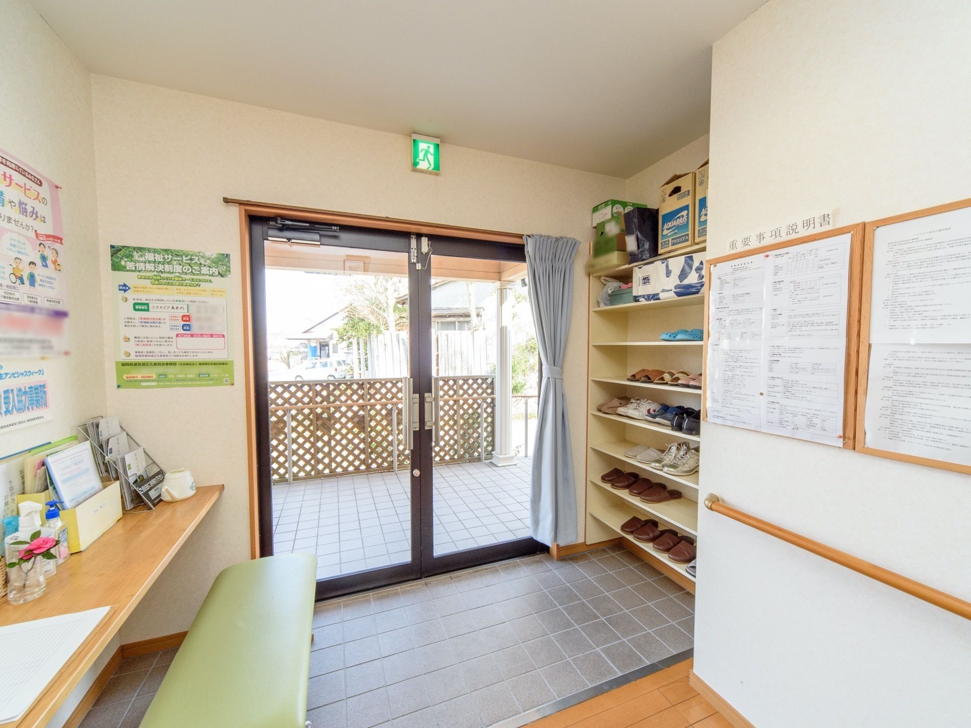 入口の右手に靴箱があり、左手には受付カウンターと緑の長椅子がある。また、壁には重要事項説明書が貼られている。