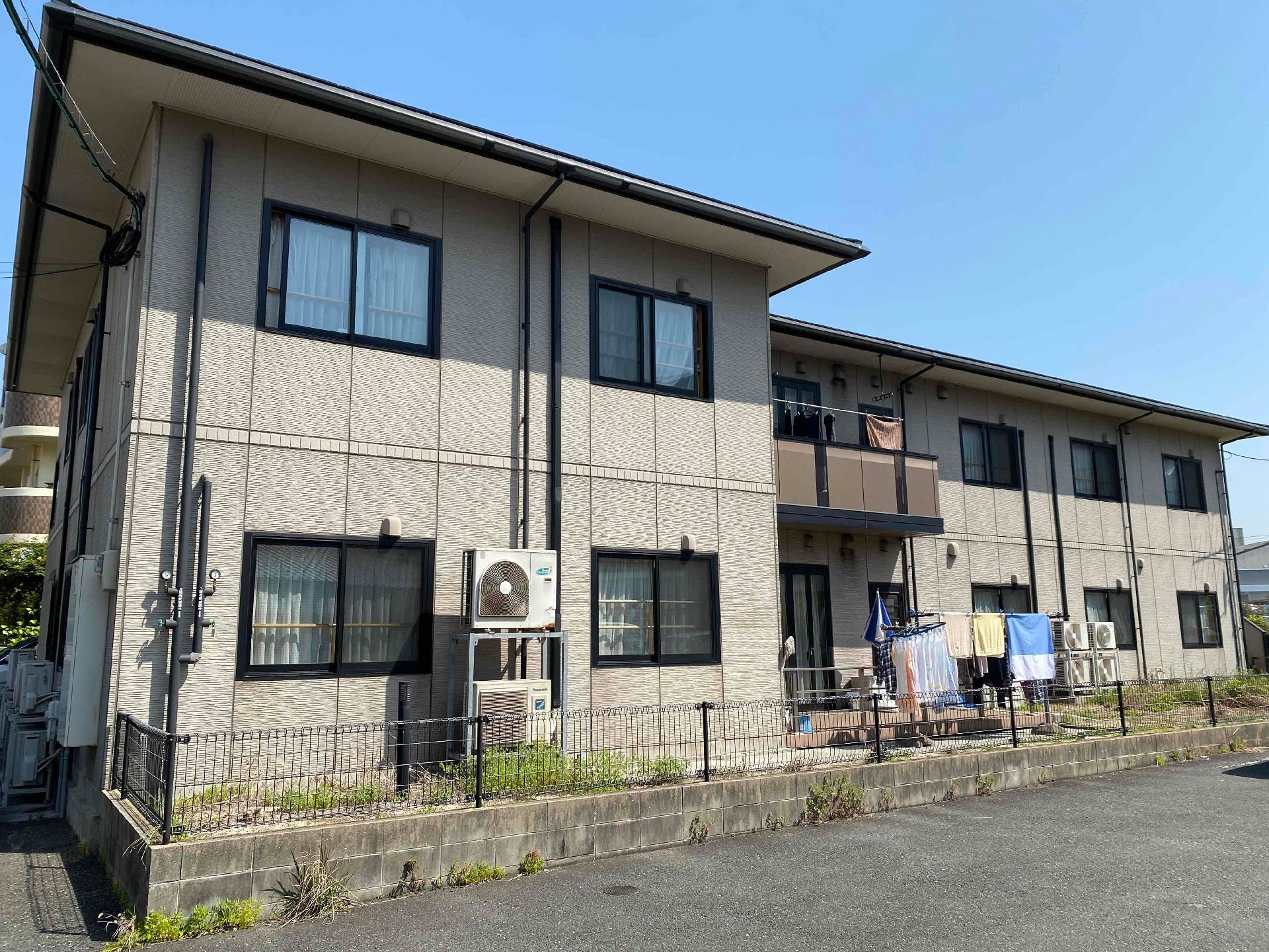 グレー系の外観の２階建ての建物は日当たり良好で、建物の2階部分にベランダがあり、屋外には洗濯物干し場がある。