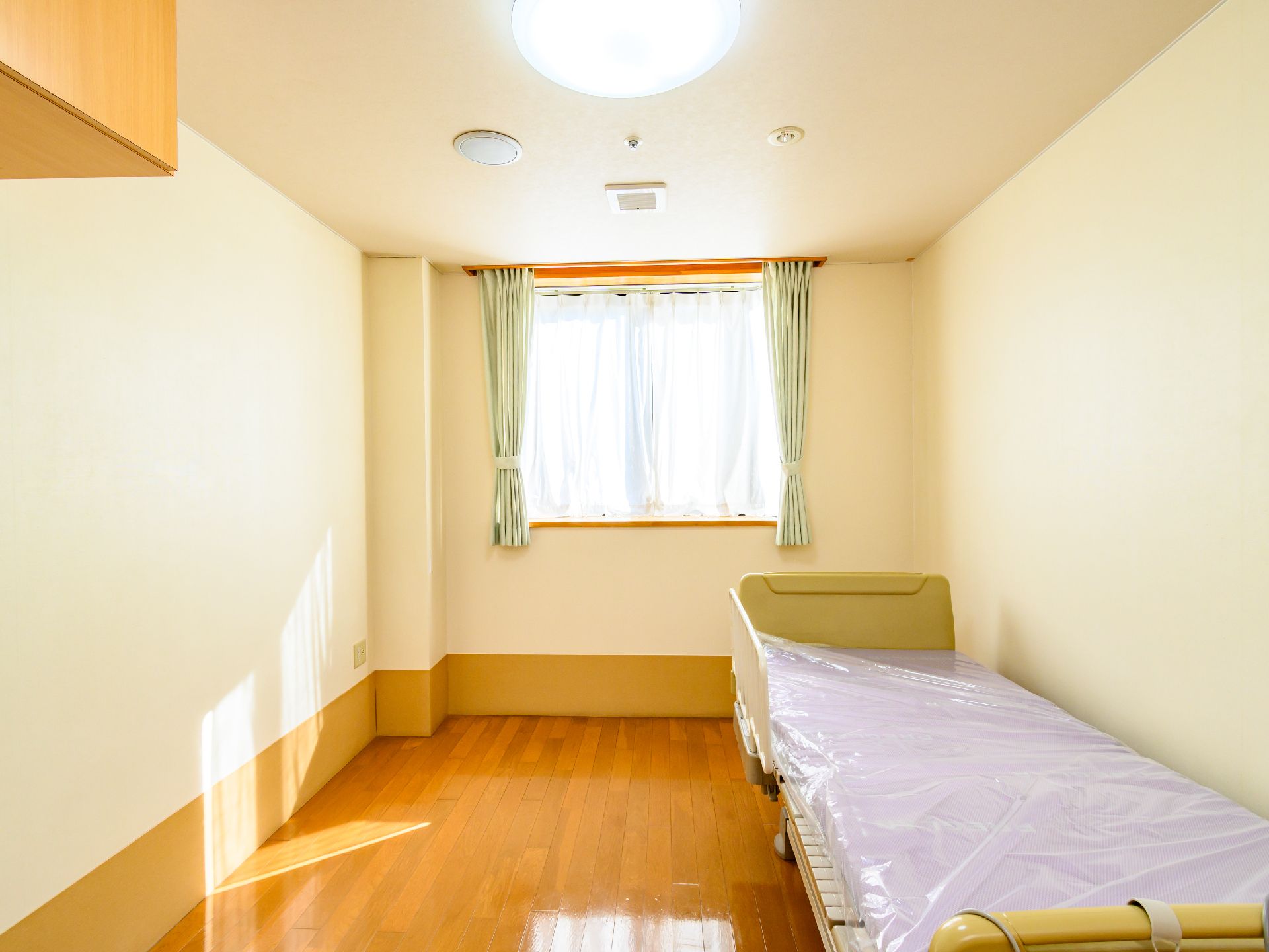 窓から日差しがあたり、介護ベッドや家具を照らしている居室