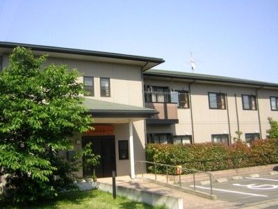ベージュを基調とした二階建ての建物。入口にはスロープがあるほか、駐車場が隣接している。