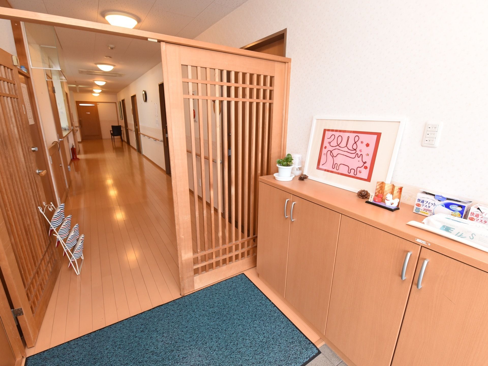 段差のない玄関。奥にスリッパたてがある。右手に収納が設置されており、上にマスクやウェットシートが置かれている。