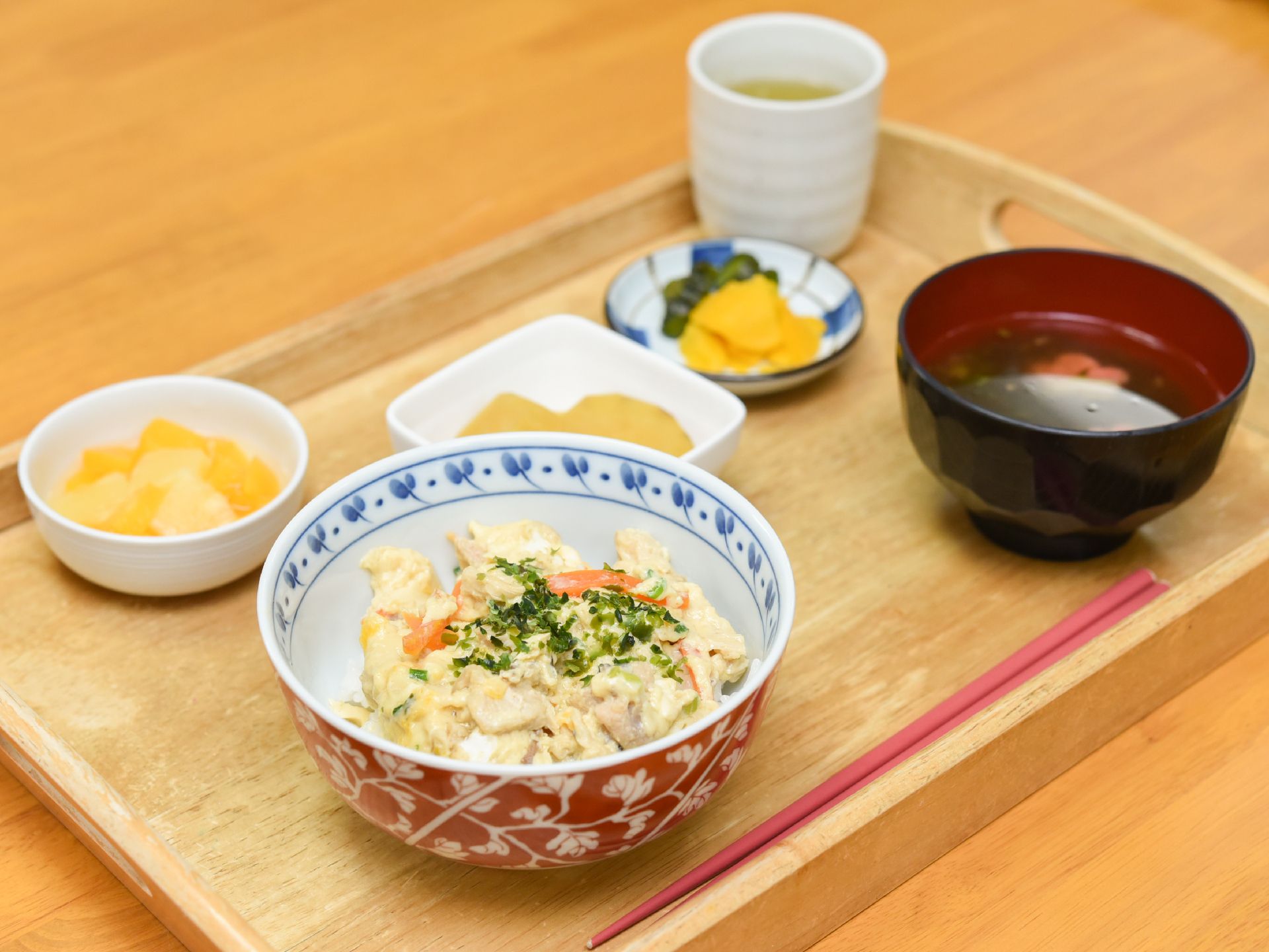 丼、汁物、副菜に漬物やデザートが置かれた木製のお盆