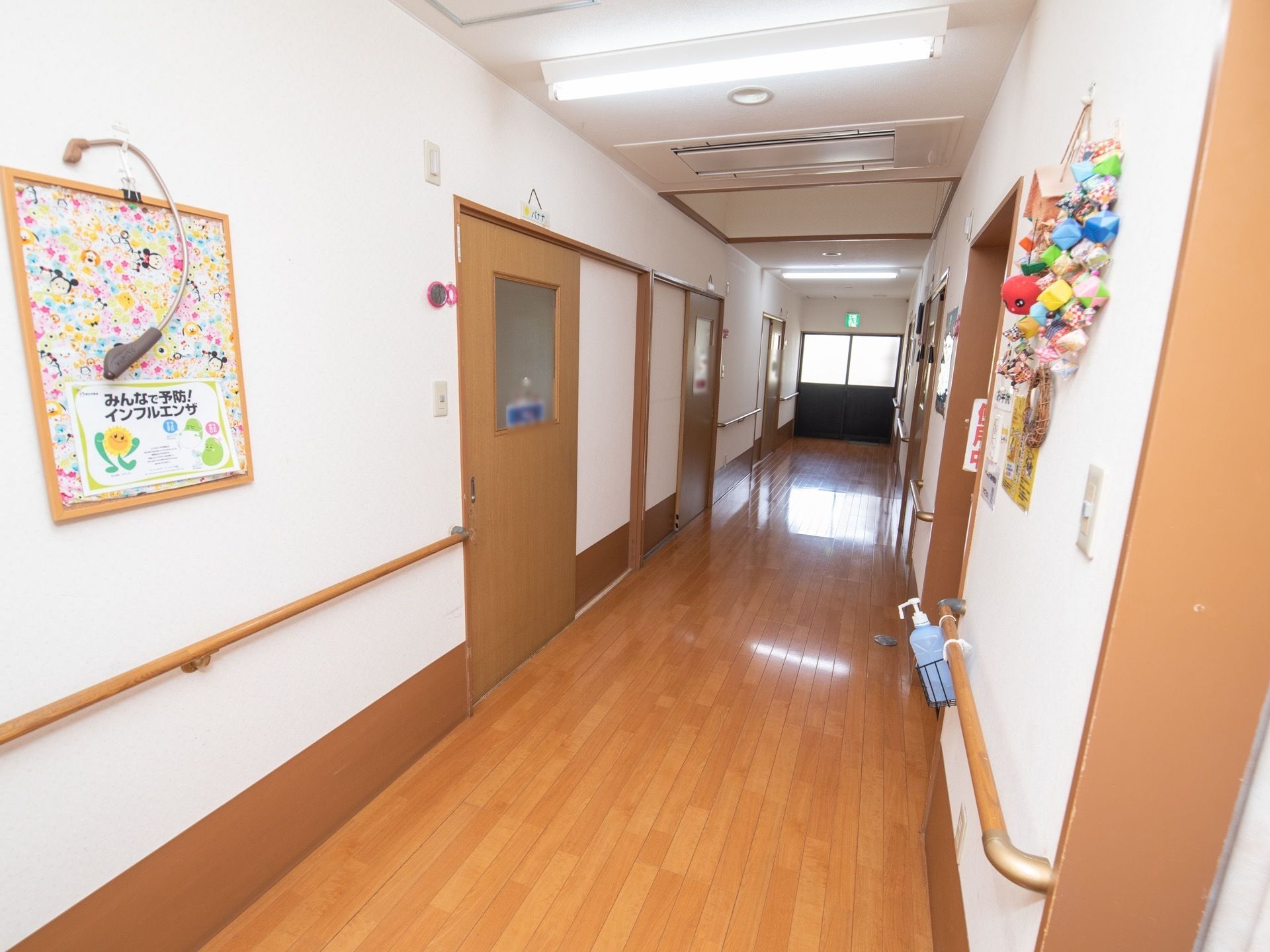 木目調に施された、フローリングの通路である。壁の両サイドに手すりが備えつけられている。掲示板が設置されている。