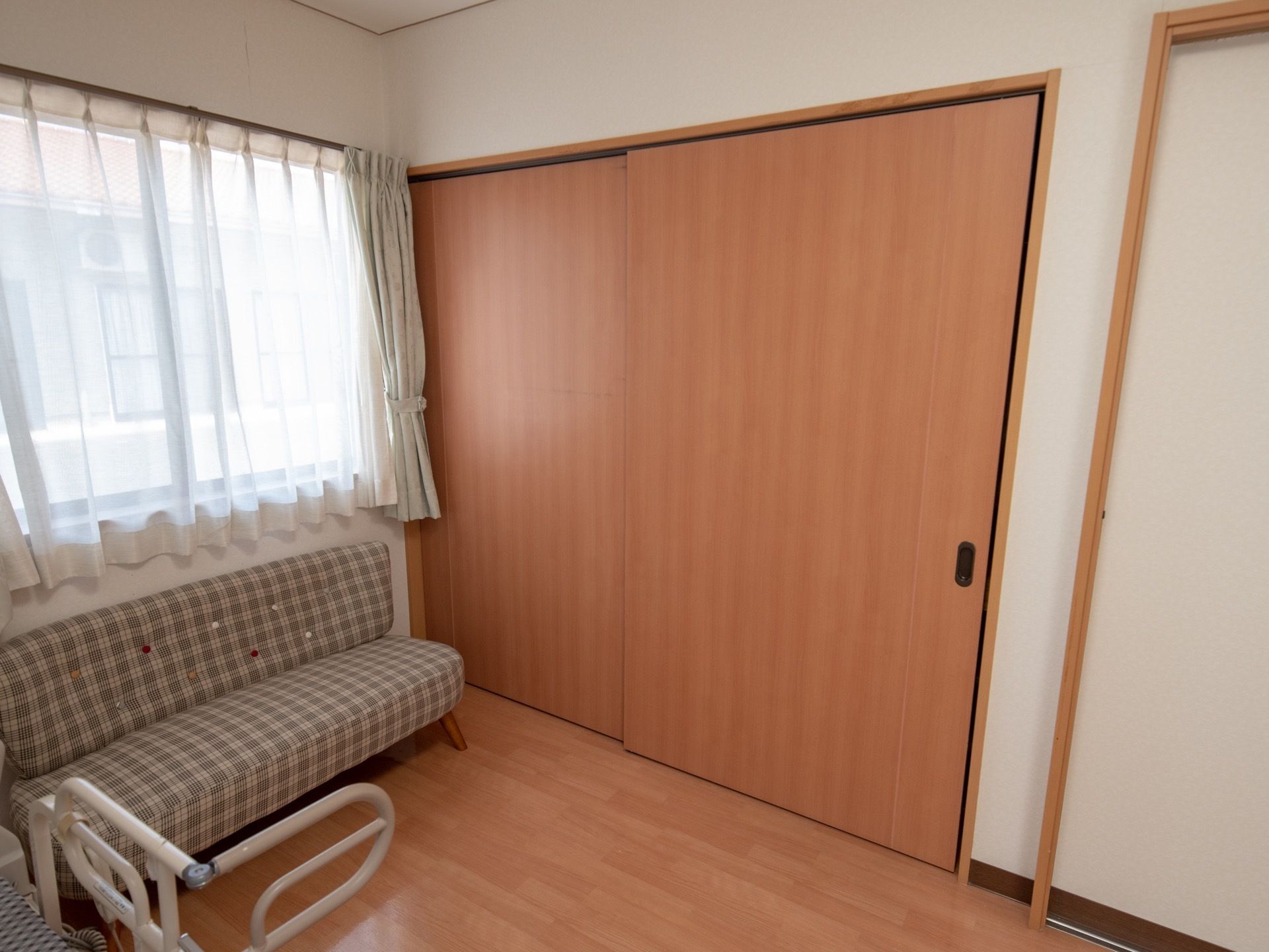 両開きの大きなクローゼットが居室に備えつけられている。手前の窓にはレースとカーテンが取りつけられている。