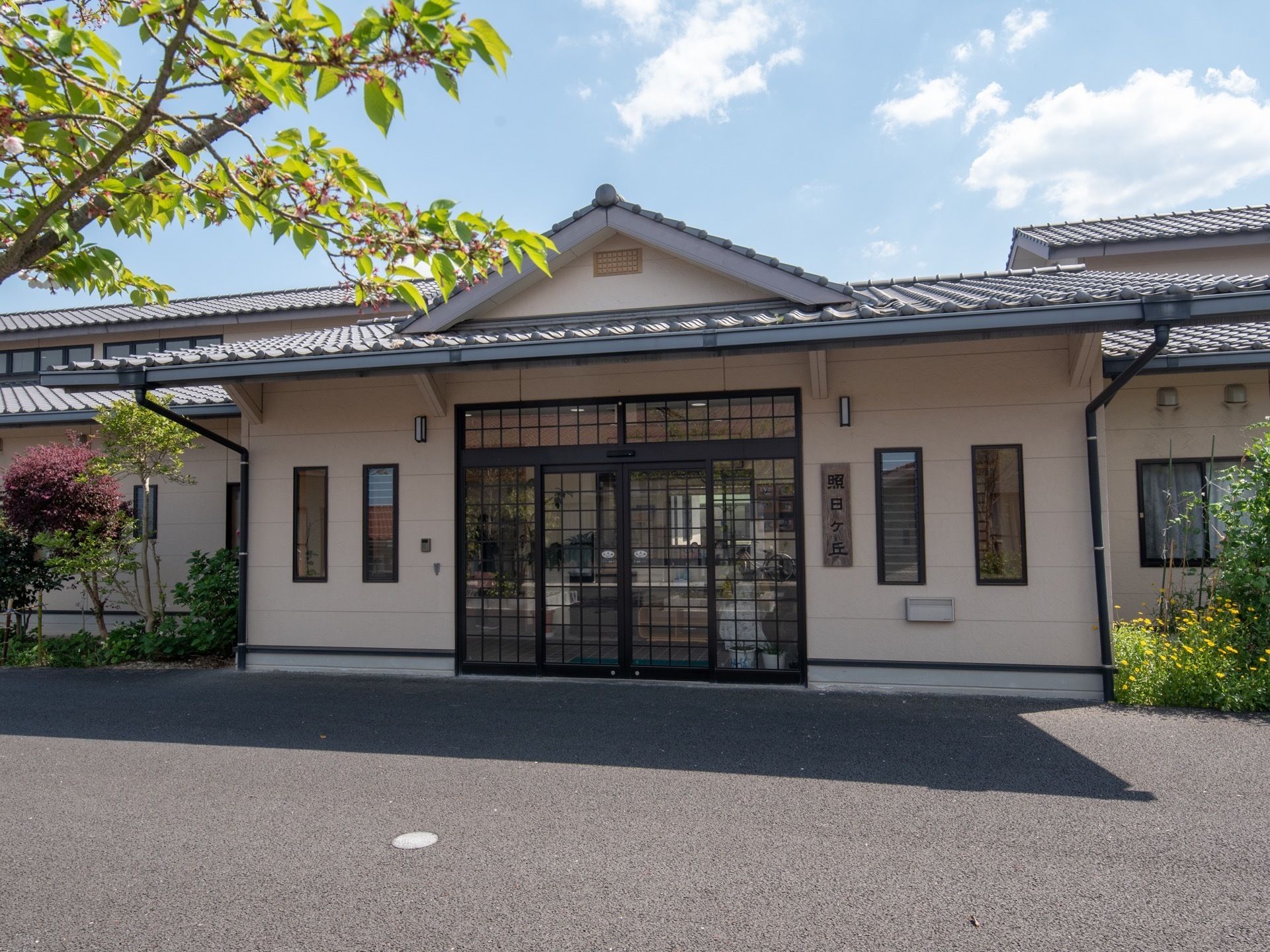 和を感じられる１階建てのグループホーム。自動ドア横の外壁には、施設名が書かれた木製の表札が掛けられている。