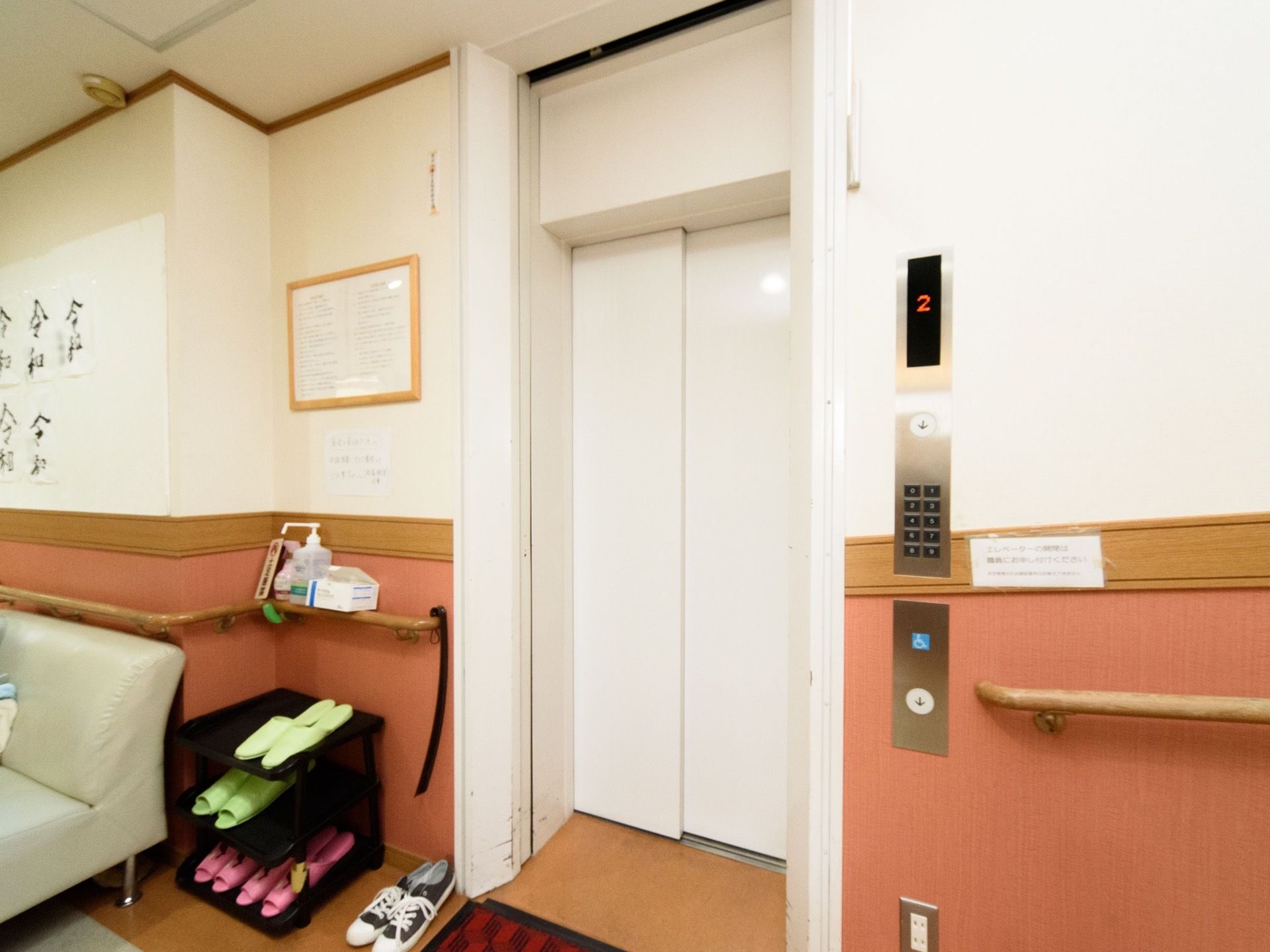 館内に完備している白いエレベーター。床にはマットがある。スリッパが用意されており、消毒スプレーが置かれている。