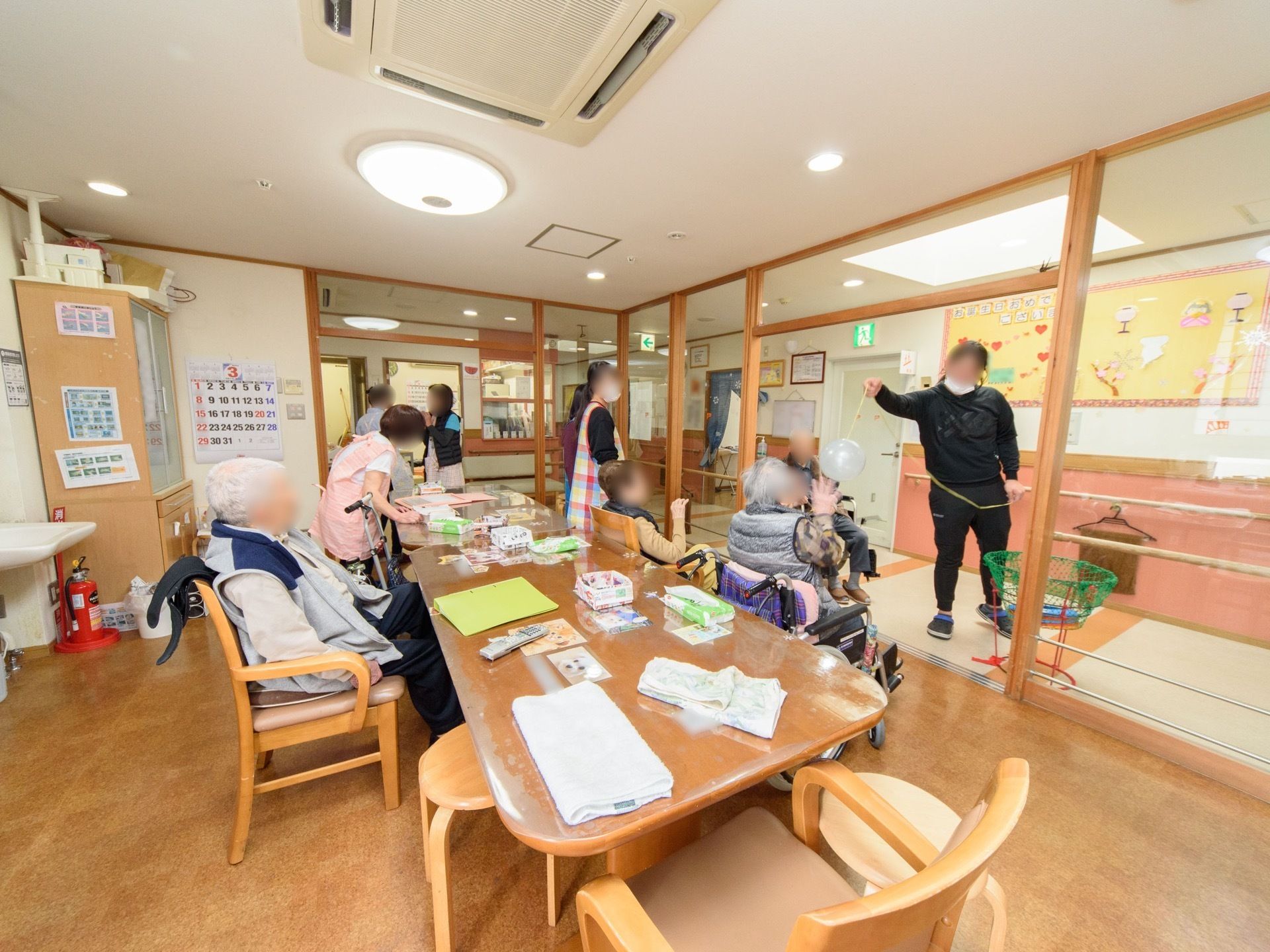 共有スペースには入居者が集まり、レクリエーション活動を行っている。廊下の壁には入居者が作成した作品が飾られている。