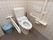 白色の洋式便座が、完備されたトイレである。壁は白色のタイル張り。可動式の手すりも備え付けられている。