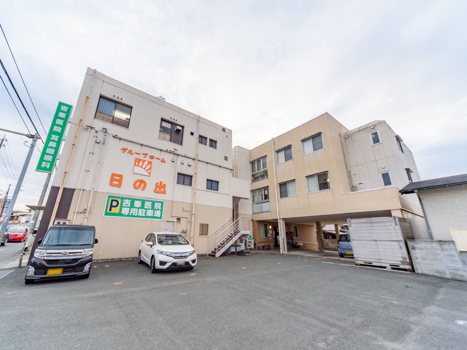 明るい色合いにデザインされた、３階建てのグループホームである。外壁に施設名が描かれている。駐車場も完備。
