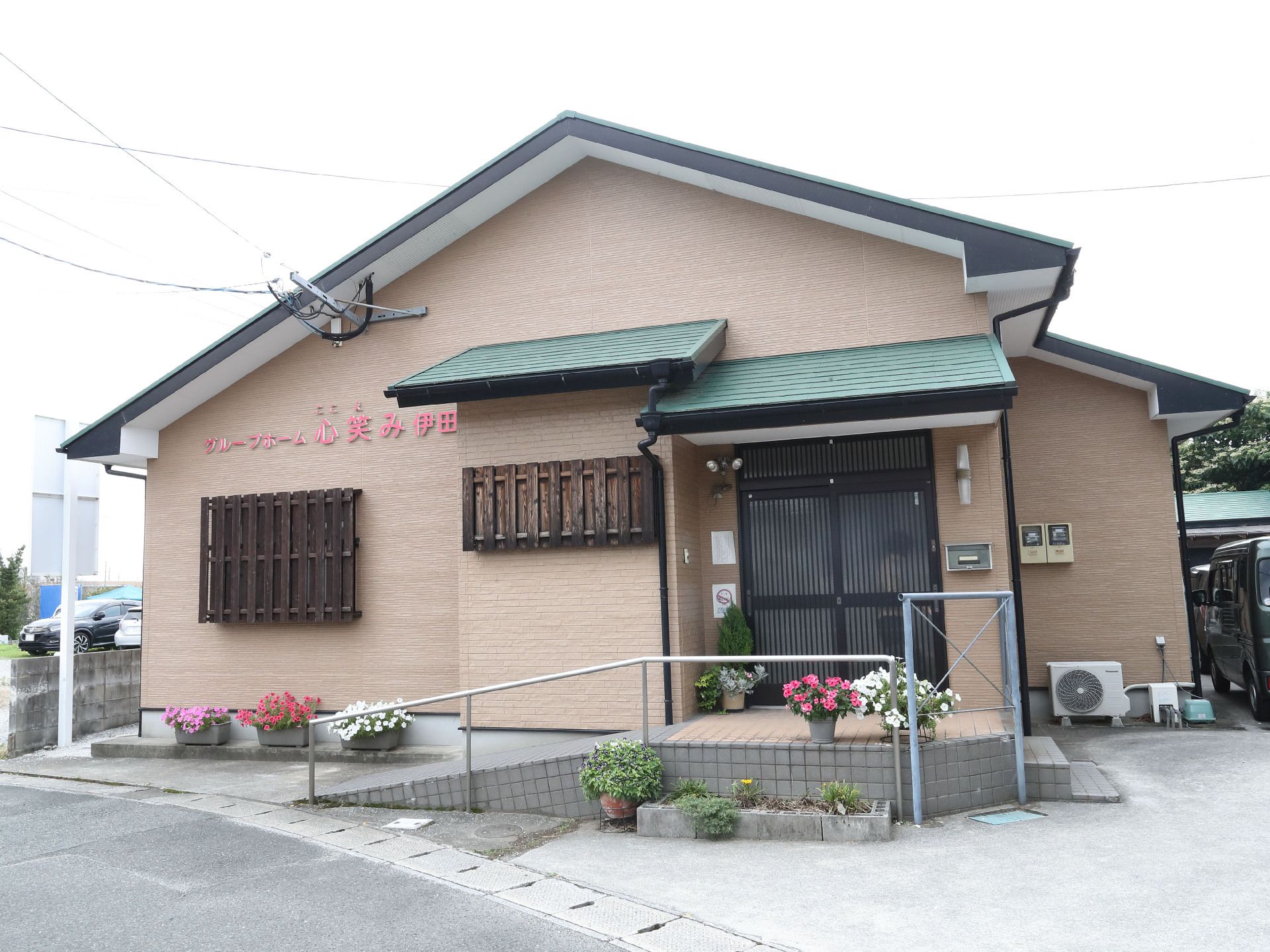アスファルトの道路沿いに立地しているスロープが付いた三角の屋根のベージュの建物