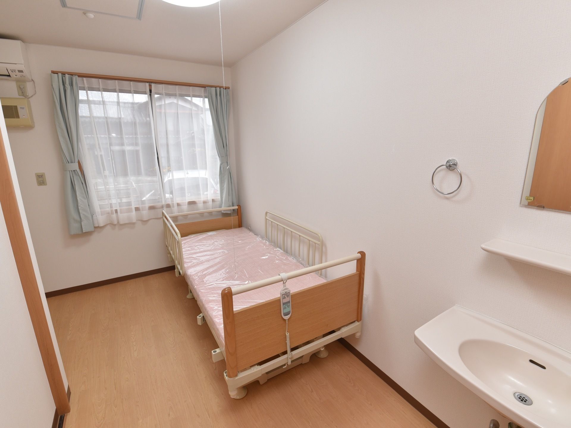 居室には電動のベッドが備えつけられている。窓からは外の光が入り、開放感がある。フローリングの床で、一人でもゆったり過ごせるスペースである。