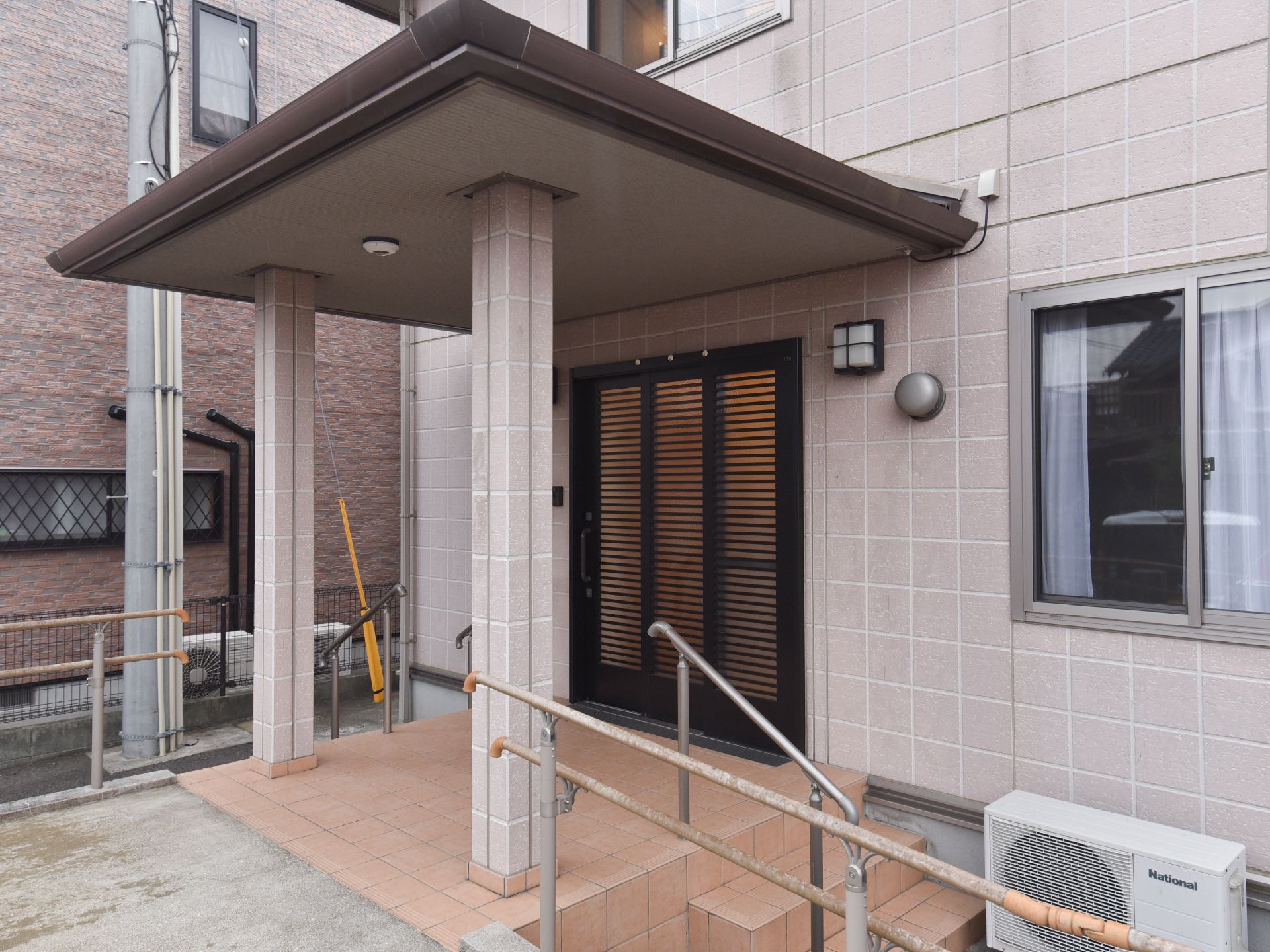 玄関周りにスロープが付いた2階建て他の建物。玄関の上には屋根が付き雨風をしのげる。