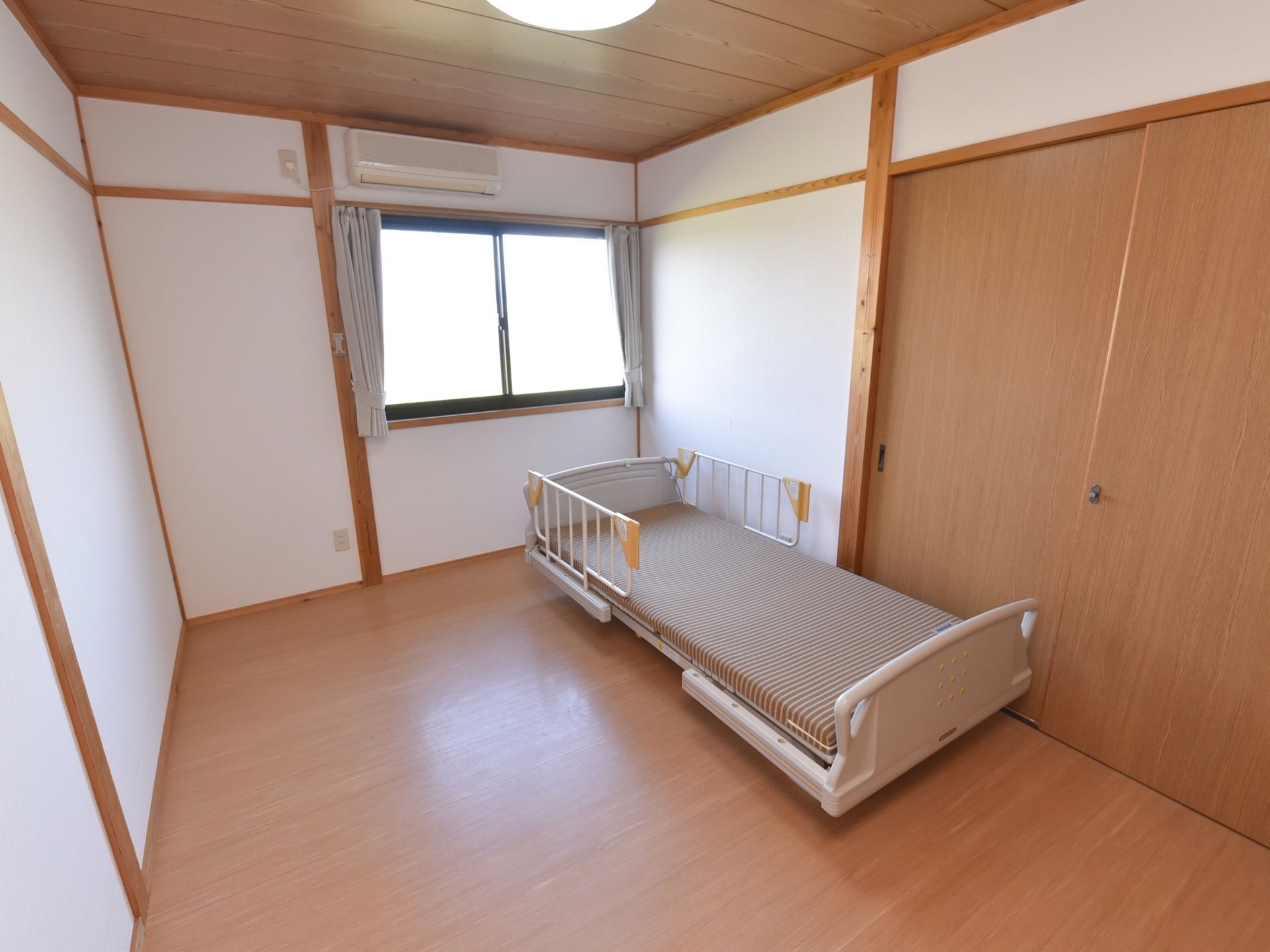 居室は広々としており、右側には柵のついたシングルベッドが置かれている。天井には、丸いシーリングライトが取りつけられている。