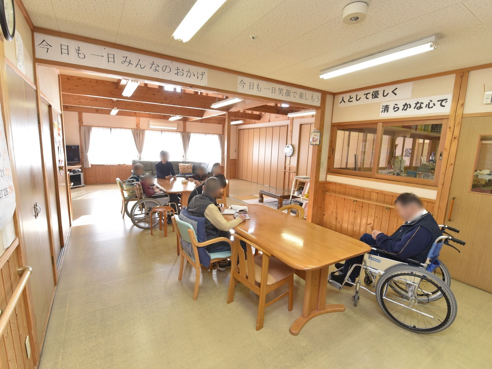 木の素材をふんだんに使用したデザインの食堂。テーブルと椅子が置かれ、一角にはガラスの窓で囲まれたスタッフルームがある。