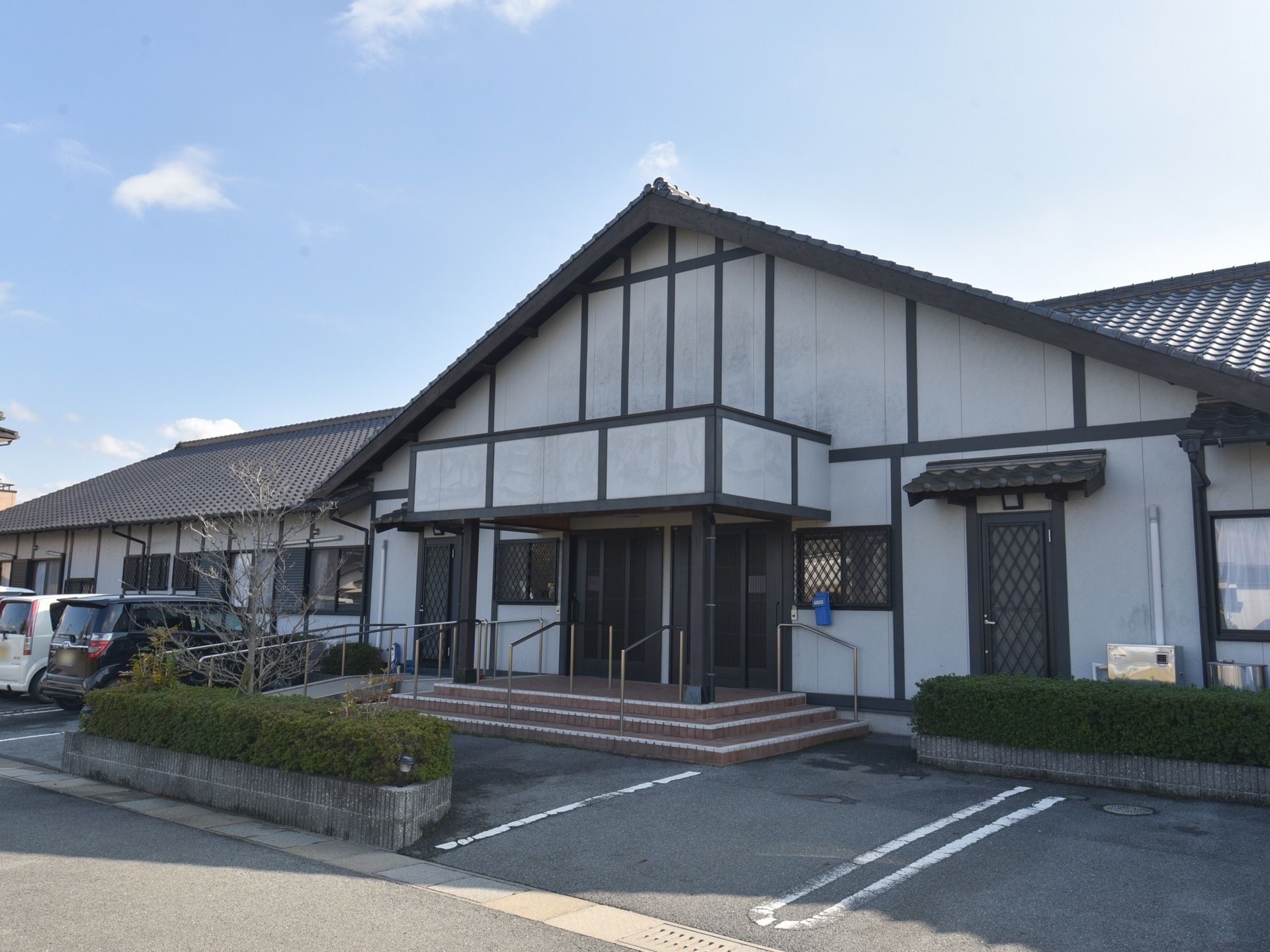 大きな平屋建ての和風の建物がある。玄関部分が大きな三角屋根になっている。玄関前は三段の階段になっており、側にはスロープがある。