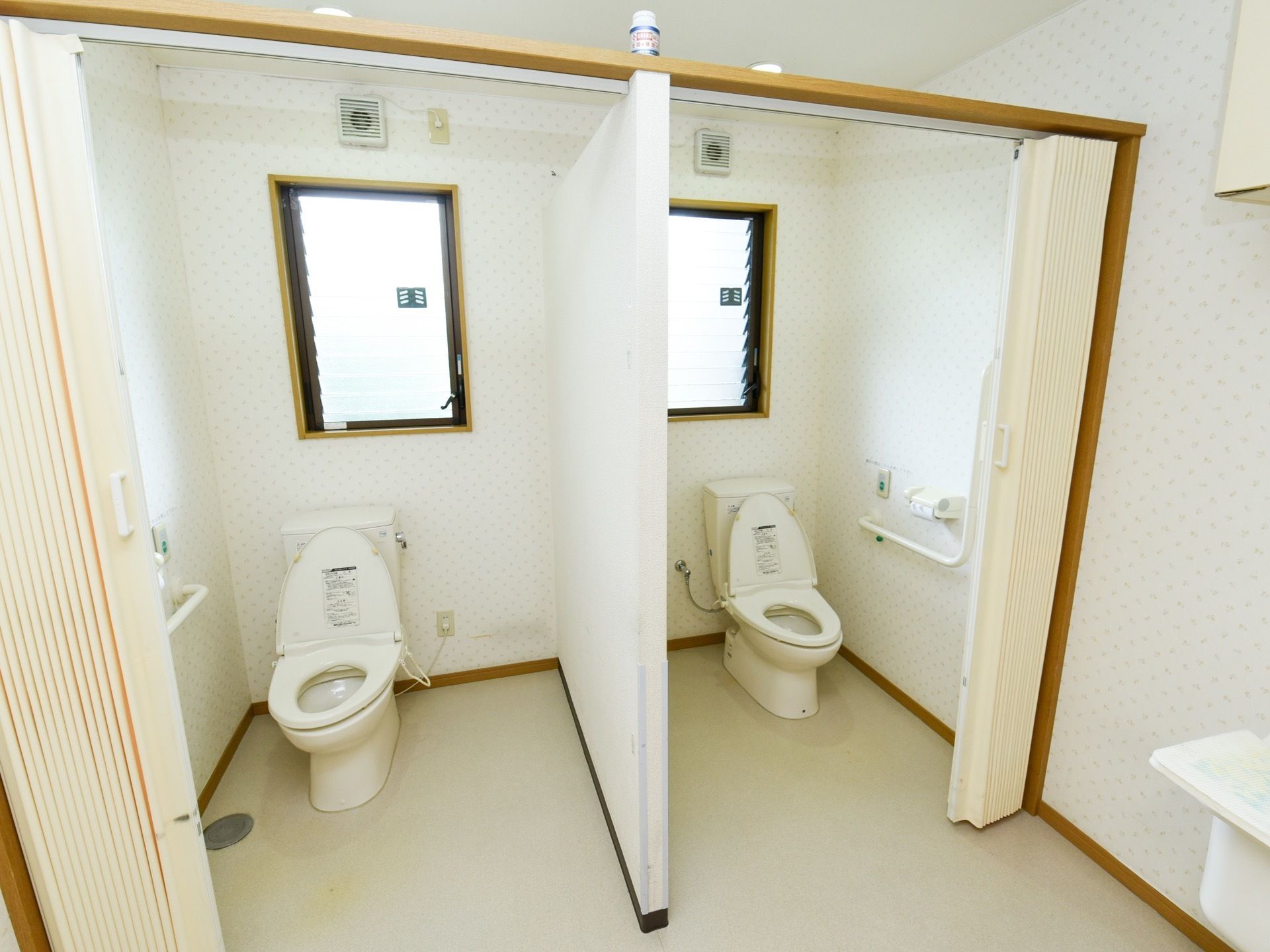 広々としたトイレである。洋式便器が壁を挟んで並んで設置されている。扉はアコーデオンカーテンになっている。