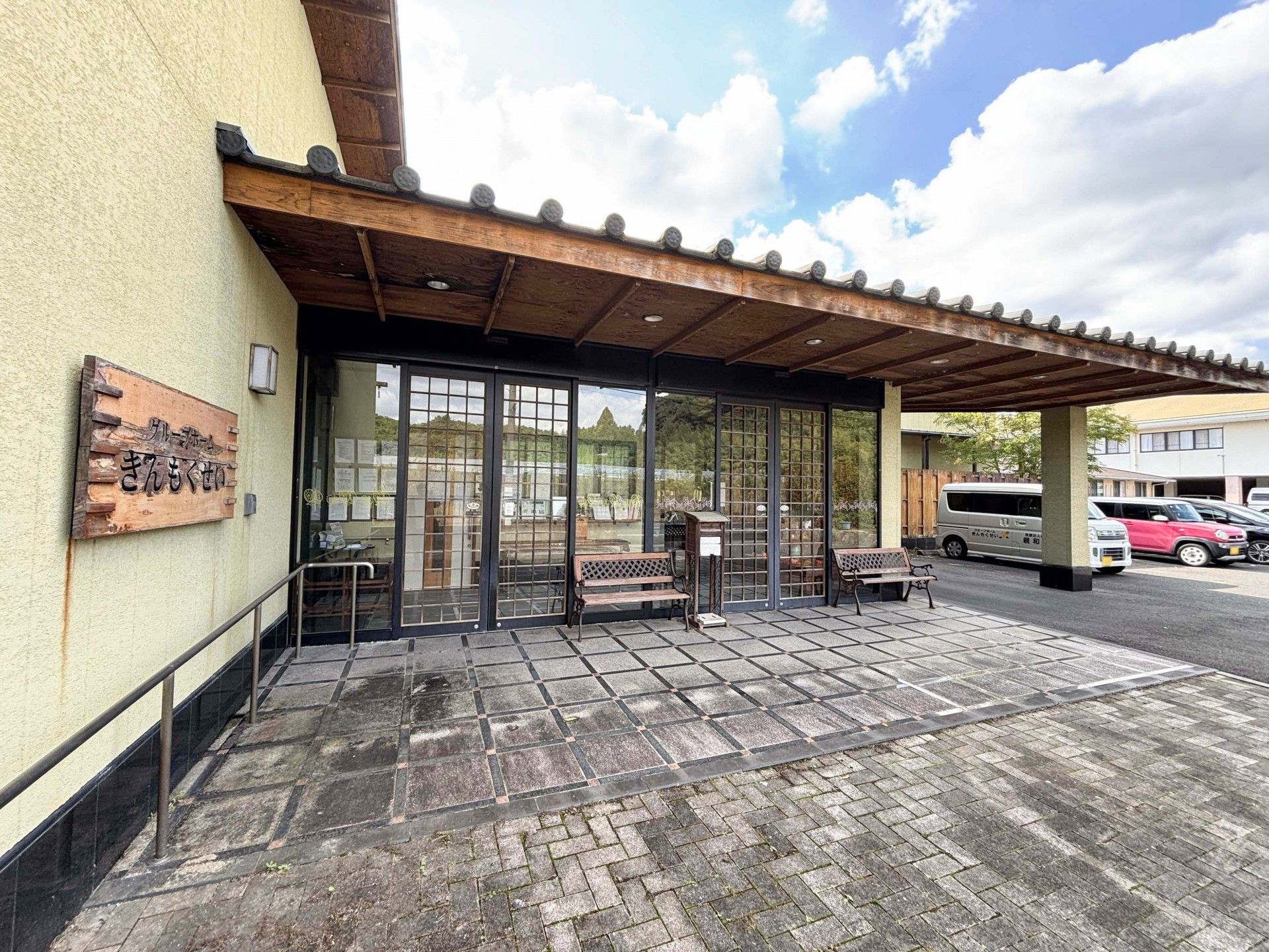 グループホーム名が書かれているベージュの外壁。平屋建ての建物にはグレーの屋根が付き、玄関先には手すり付きのスロープがある。