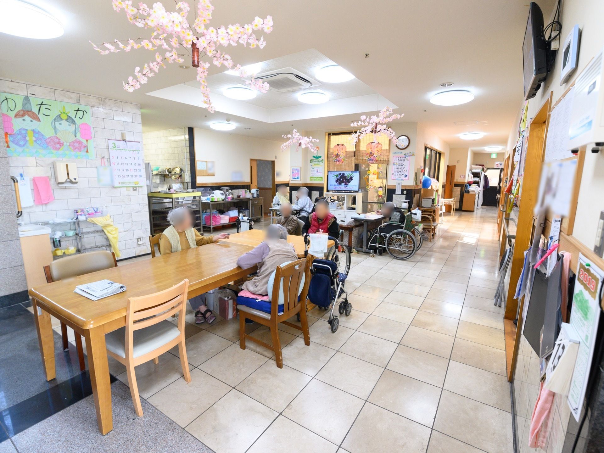 長方形のテーブルと、小さめのテーブルがくっついて置いてある。天井には、ピンク色で放射線状に開いている造花が3か所吊るされている。