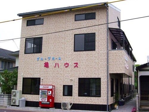 ベージュの建物の前には自動販売機が設置されている。住宅地の一角にあり、アットホームな雰囲気。