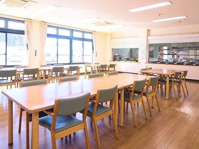 奥にキッチンスペースがある食堂の様子。広めの空間に長い机と椅子がたくさん並んでいる