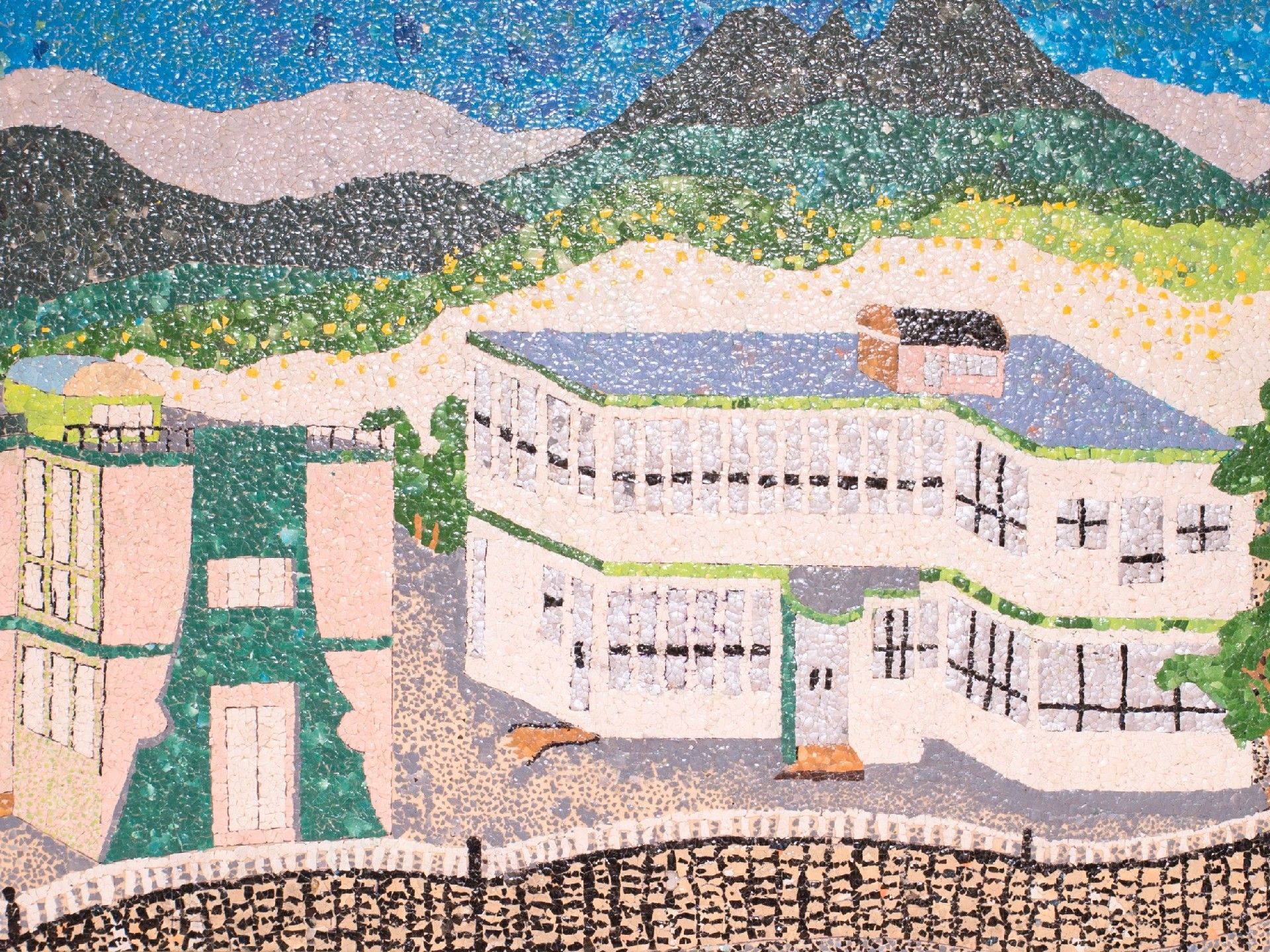 貼り絵のようなモザイク画。手前に学校やマンションのような建物。向こうに山々が見える。