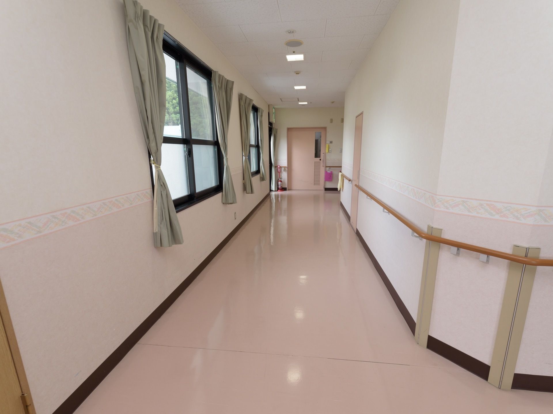 廊下の床面は、ピンク色のビニール素材である。窓と反対側の壁には、コーナー部分も切れ目なく手すりが設置されている。