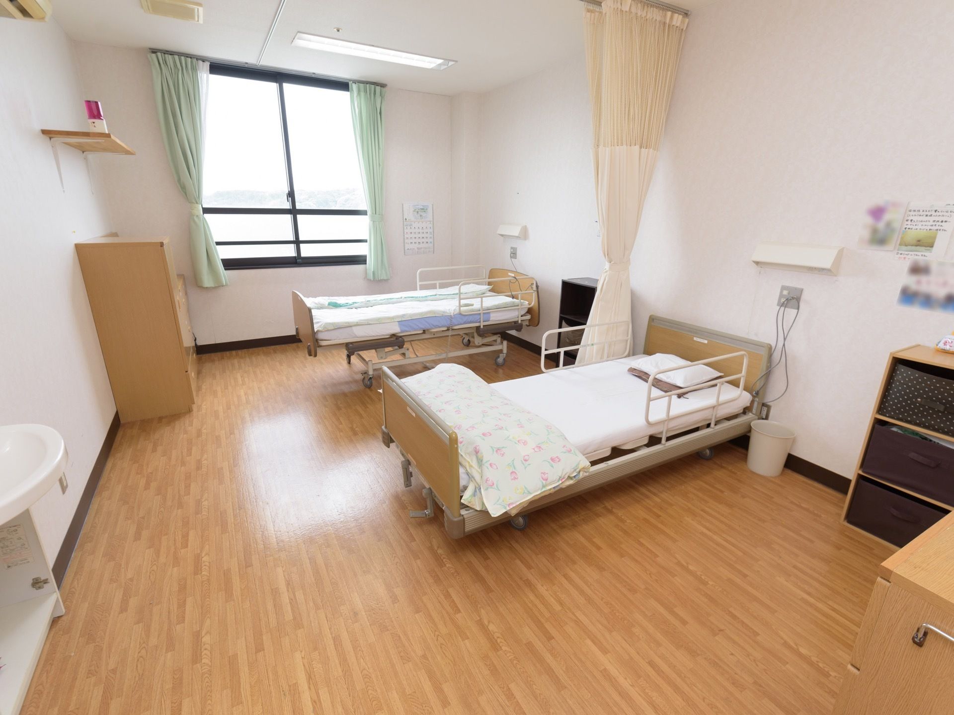 ２人用の居室に、転落防止柵のついたベッドが２台設置されている。緊急を知らせる赤色灯が、壁に取りつけられた棚板の上に置かれている。