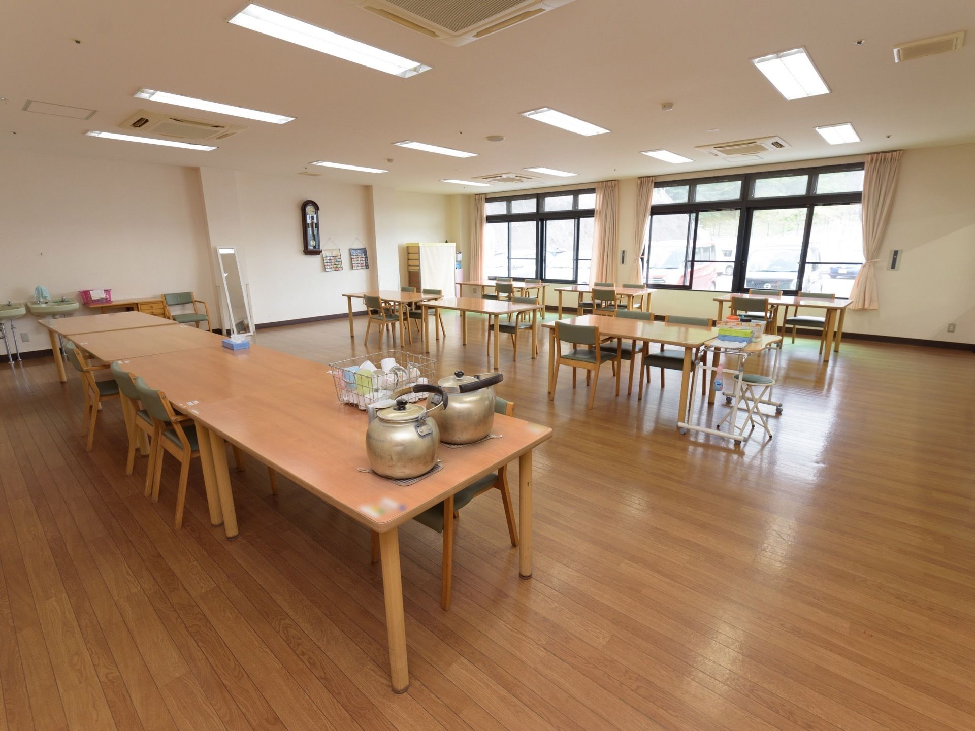 食堂のテーブルに、大きなやかんが２つ置かれている。その横に、多くのコップがかごに入れて乾かされている。