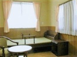 大きな窓が二つ付いた居室には手すり付きのベッドがあり、テーブルセットも置かれている。