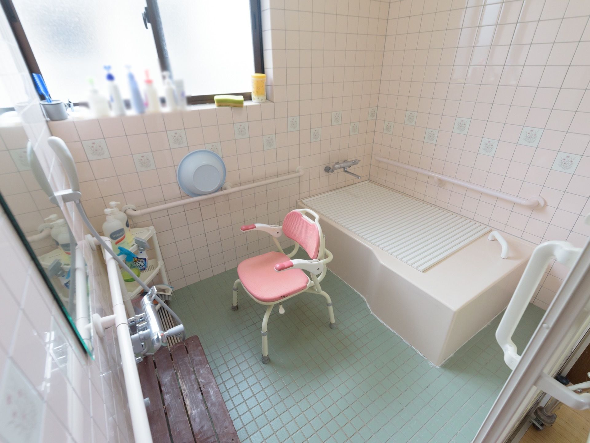 床と壁にタイルが貼られた浴室で、床は水色、壁はピンクのものが使用されている。右奥に浴槽があり、ふたが閉められている。