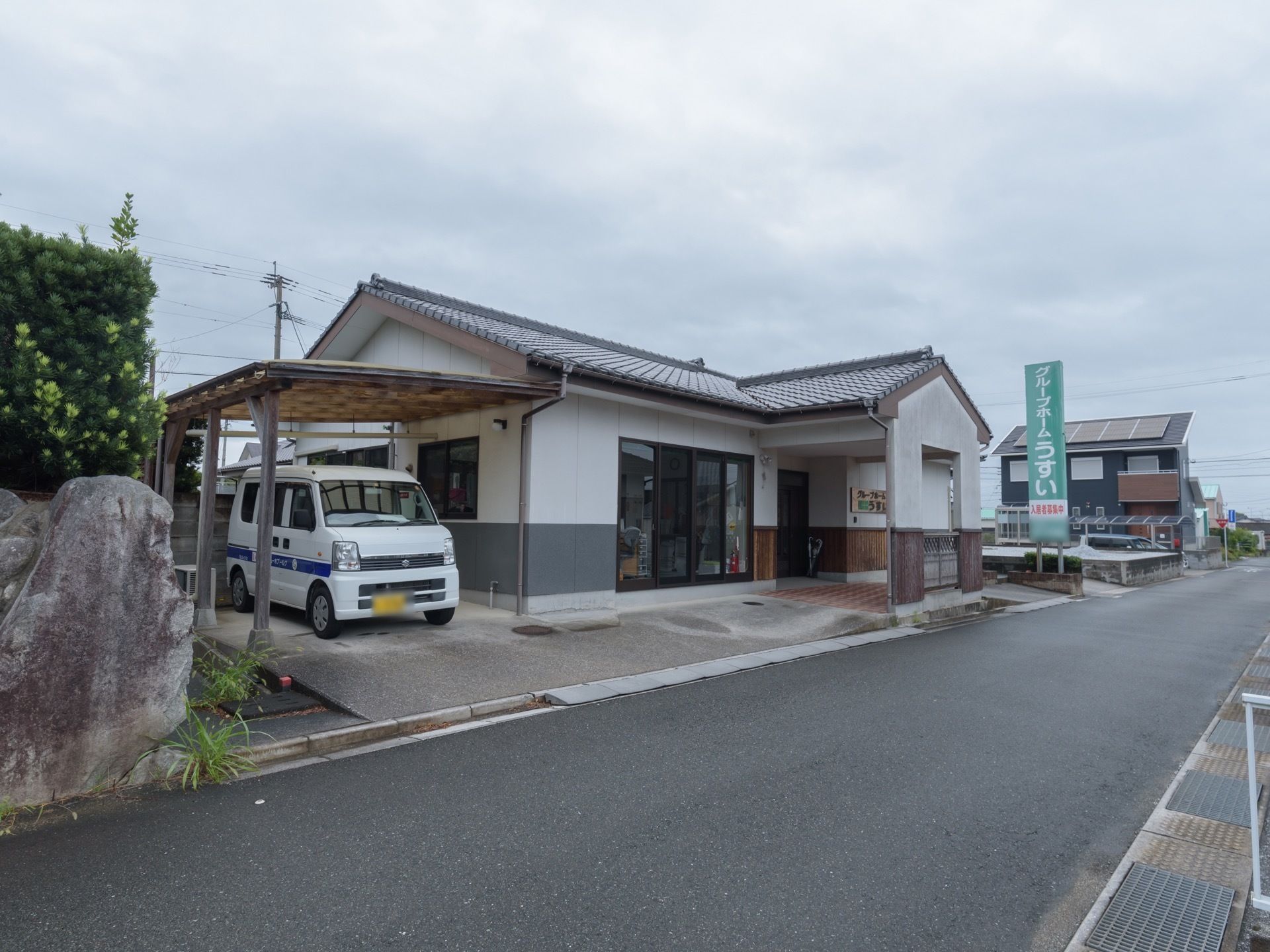 平屋建ての建物になっている。駐車場には車が1台停められている。施設名が記された看板がある。