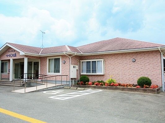 ピンクの外壁の平屋建ての建物。外壁にはホーム名が書かれている。玄関先には手すり付きのスロープもある。