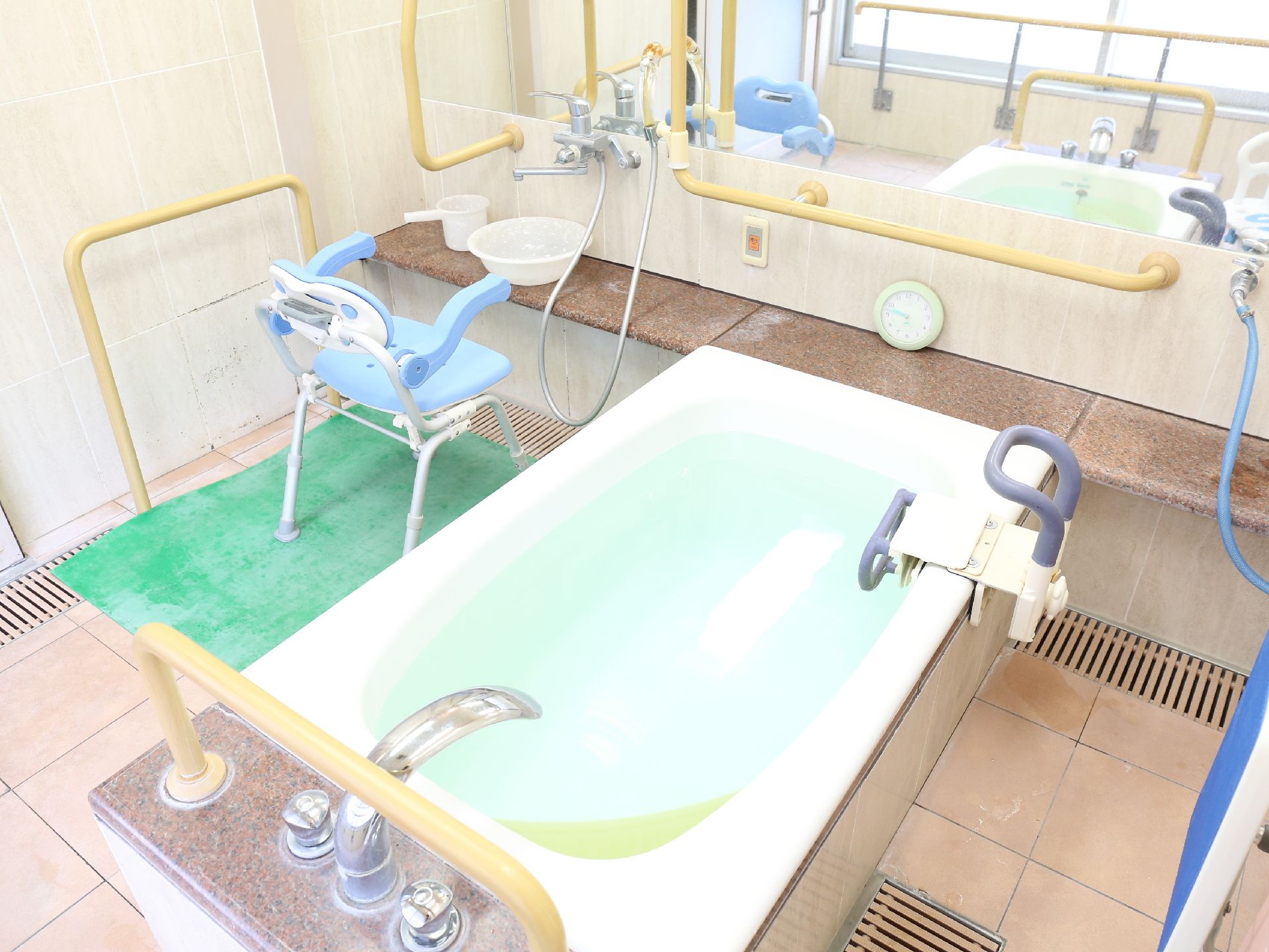 浴室内には、黄色い手すりが設置されている。シャワーの前には、青い肘おきが付いた椅子が置かれており、座って体を洗うことが出来る。