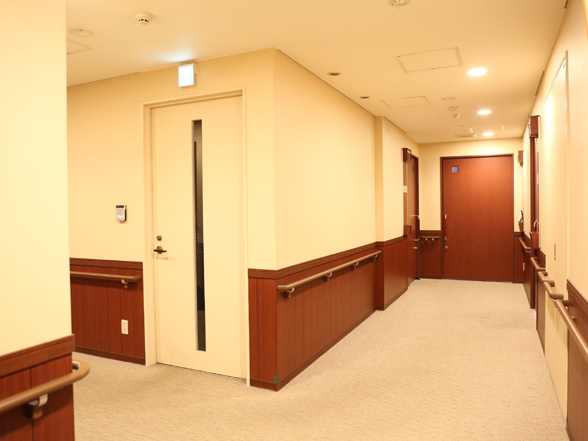 廊下に並んでいる居室のドアは焦げ茶色だが、非常口のドアは白であり、目立つ。廊下の壁には手すりが取り付けられている。