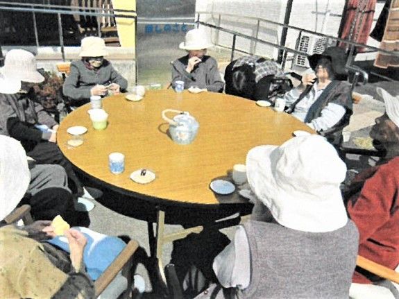 丸テーブルにすわって日光浴しながら話をしている高齢者の様子