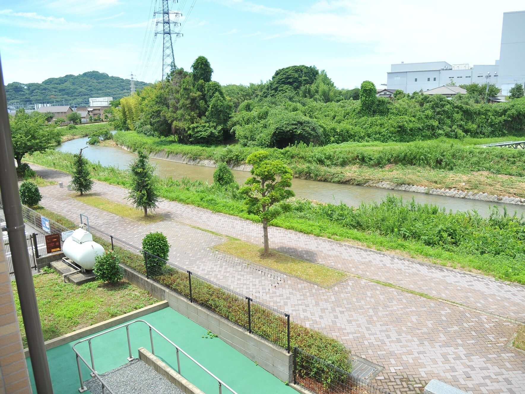 川が流れ、緑が多く残る地域。川上の方には住宅地もあり、その後ろには山がある。右川には白いい大きな建物が建っている。